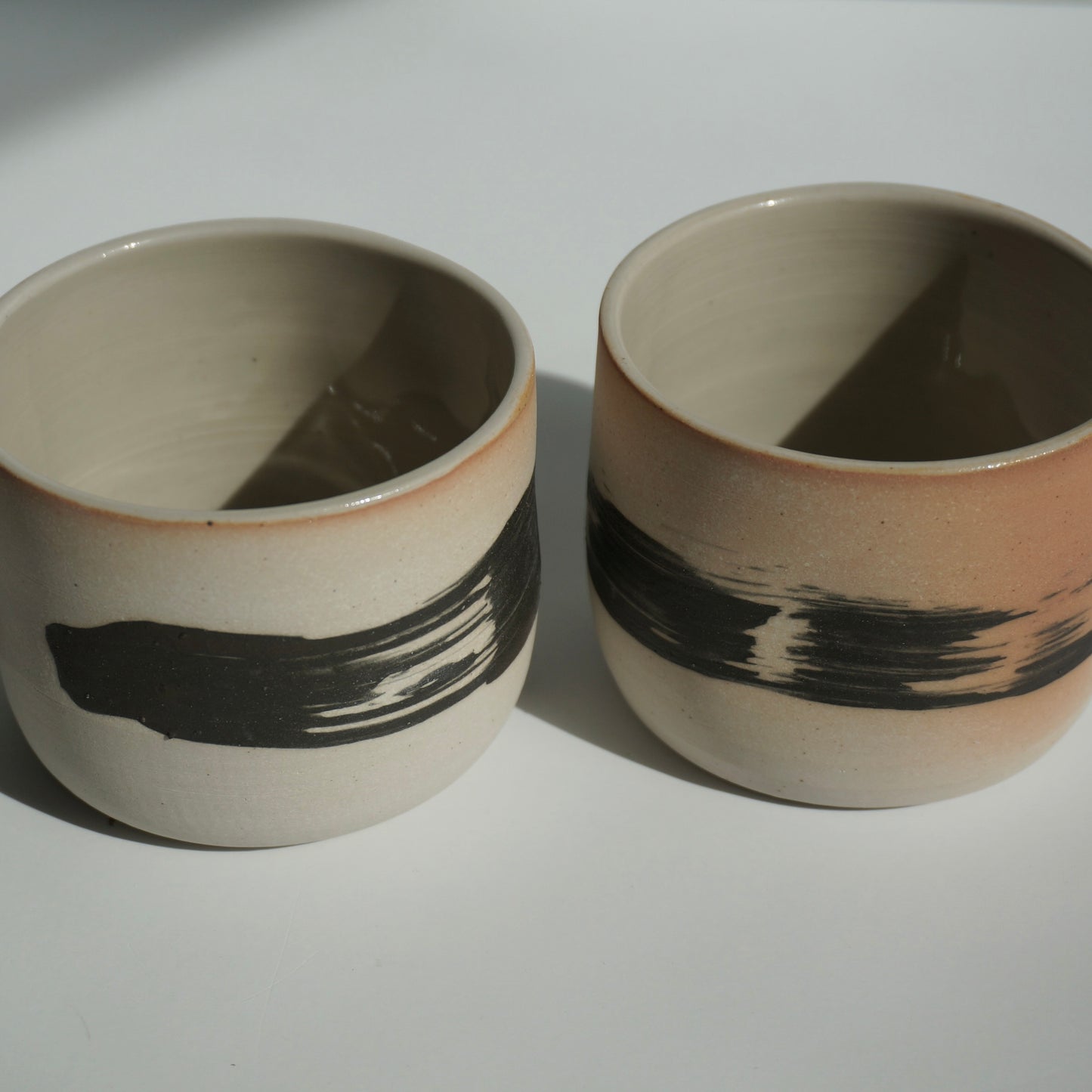 Two handmade ceramic cups with black brushstrokes by Kongji Pottery