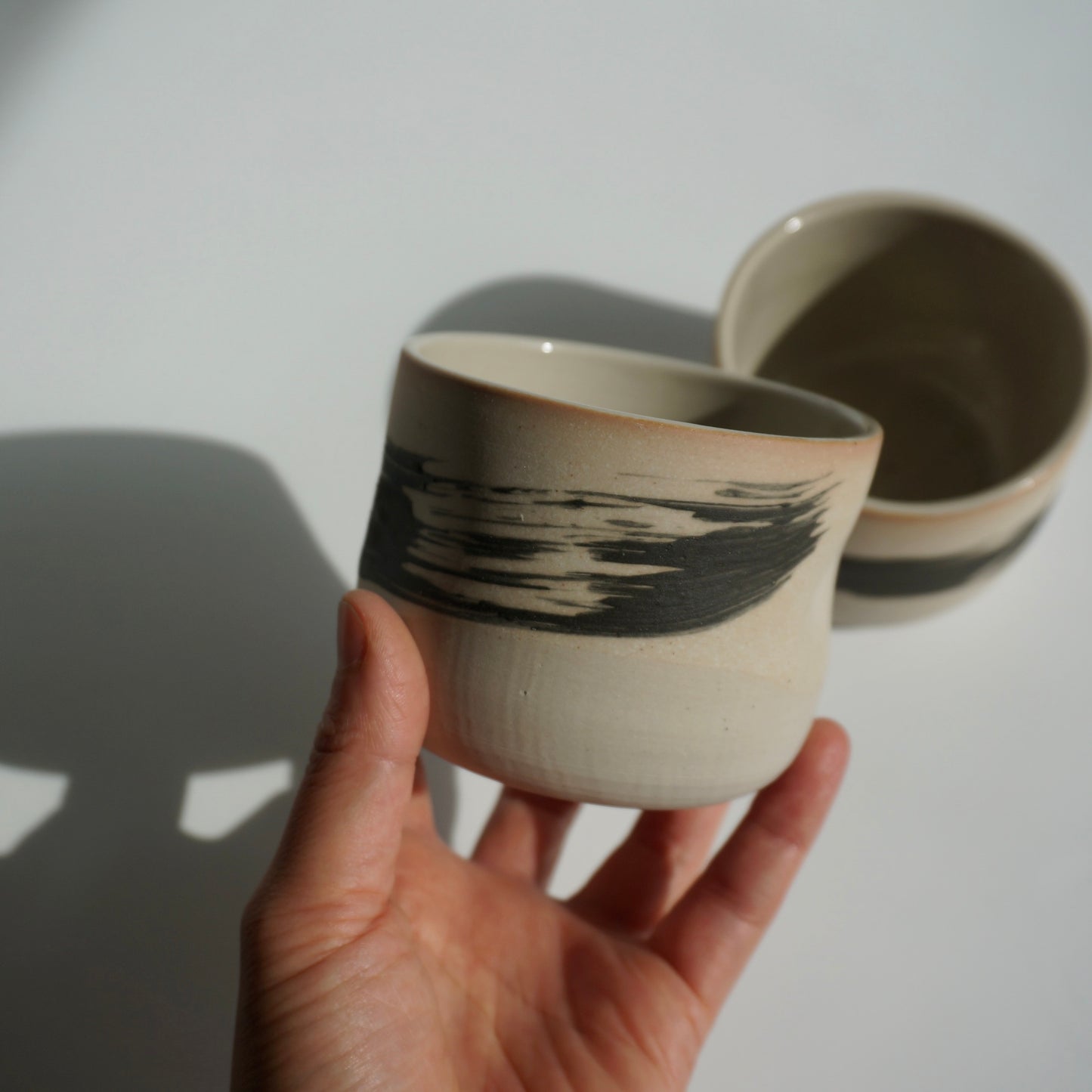 Hand holding a handmade ceramic cup with black abstract brushstroke