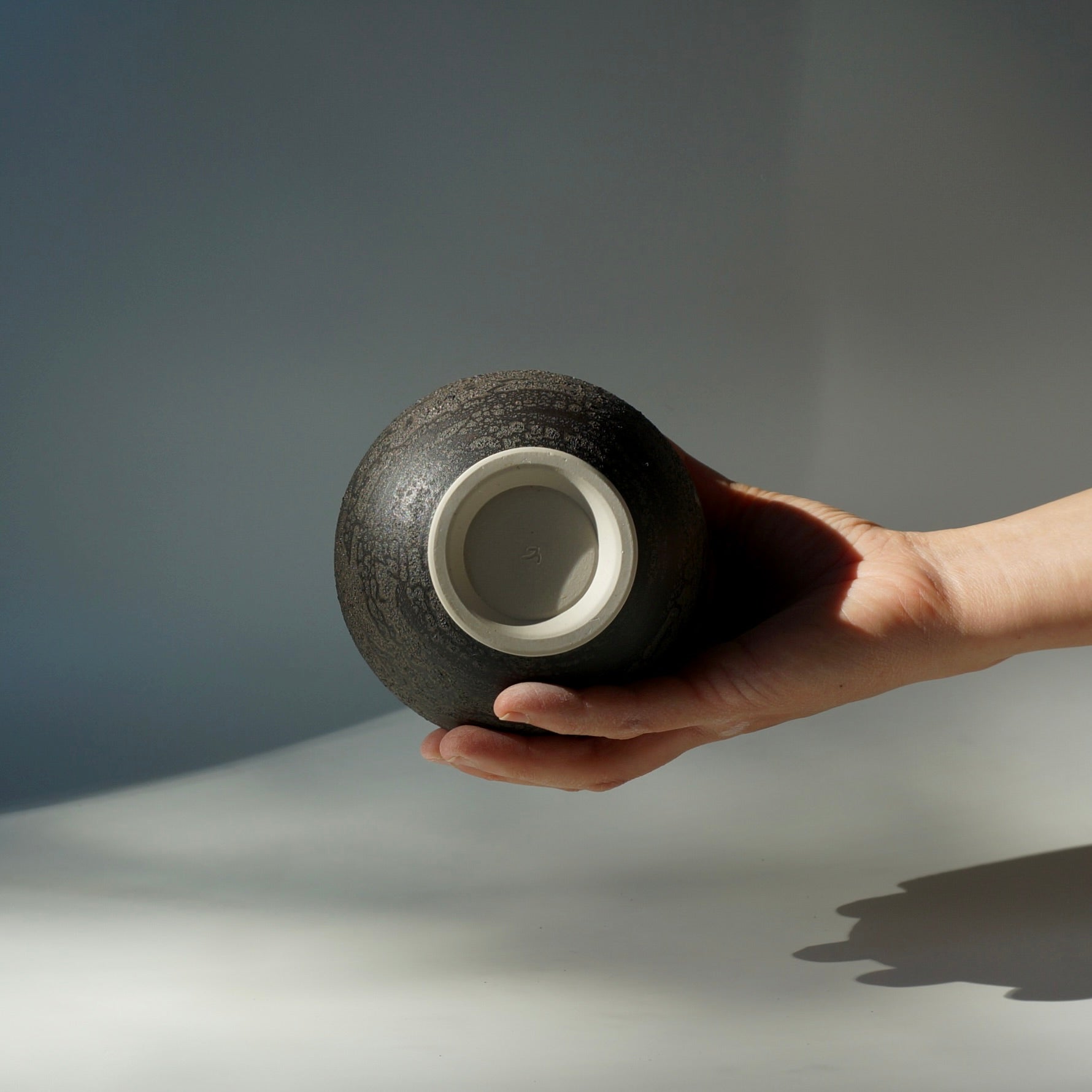 Hand holding a textured black handmade ceramic moon jar by Kongji Pottery